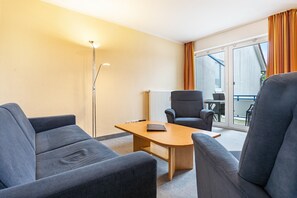 Una habitación de hotel con sofá, sillón y una pequeña mesa con un libro.