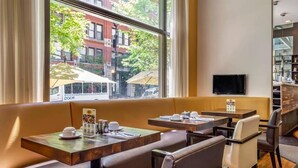 Un restaurant avec des banquettes et des tables, un téléviseur accroché au mur et une vue sur les bâtiments environnants.
