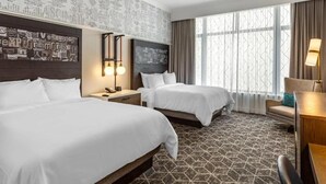 Une chambre d’hôtel avec deux lits, une grande fenêtre avec des rideaux, un mur orné de texte et une moquette à motifs.