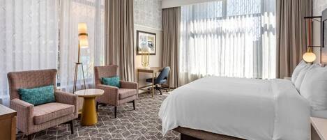 A hotel room with a large bed, two armchairs, a small round table, and a desk with a chair.