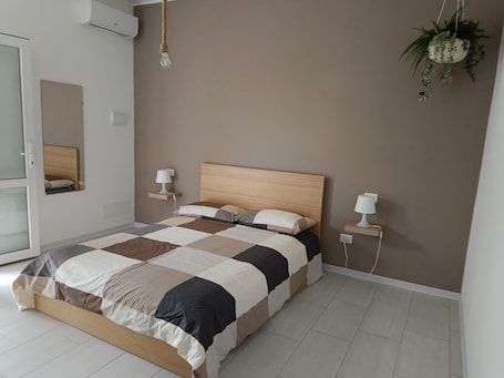 A bedroom with a wooden bed, a checkered bedspread, bedside lamps, a hanging plant, and a mirror.. Room in Villa with Pool, Wi-Fi and Air Conditioning