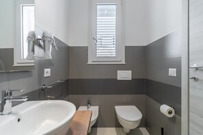 A bathroom with a sink, bidet, toilet, and a window with blinds. - Room in villa with garden, Wi-Fi and air conditioning (Solarino)