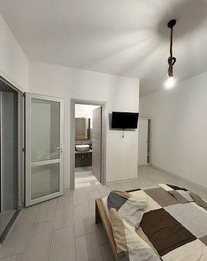 Camera da letto moderna con un letto, una televisione e un bagno visibile attraverso una porta aperta.