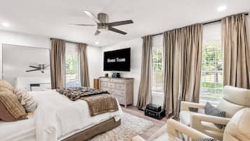Une chambre moderne avec un lit, une télévision, un ventilateur de plafond et une vue sur la verdure environnante.