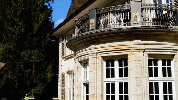 An outdoor dining area with tables and chairs, a building with classical architecture, and a large tree in the background. - Landsitz Kammerburg - Villa (Lorch)