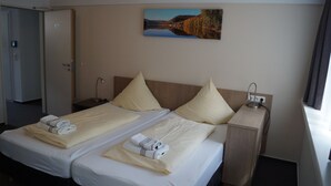 A hotel room with two beds, a nightstand, a lamp, a painting on the wall, and a window with curtains. - Landsitz Kammerburg - Villa (Lorch)