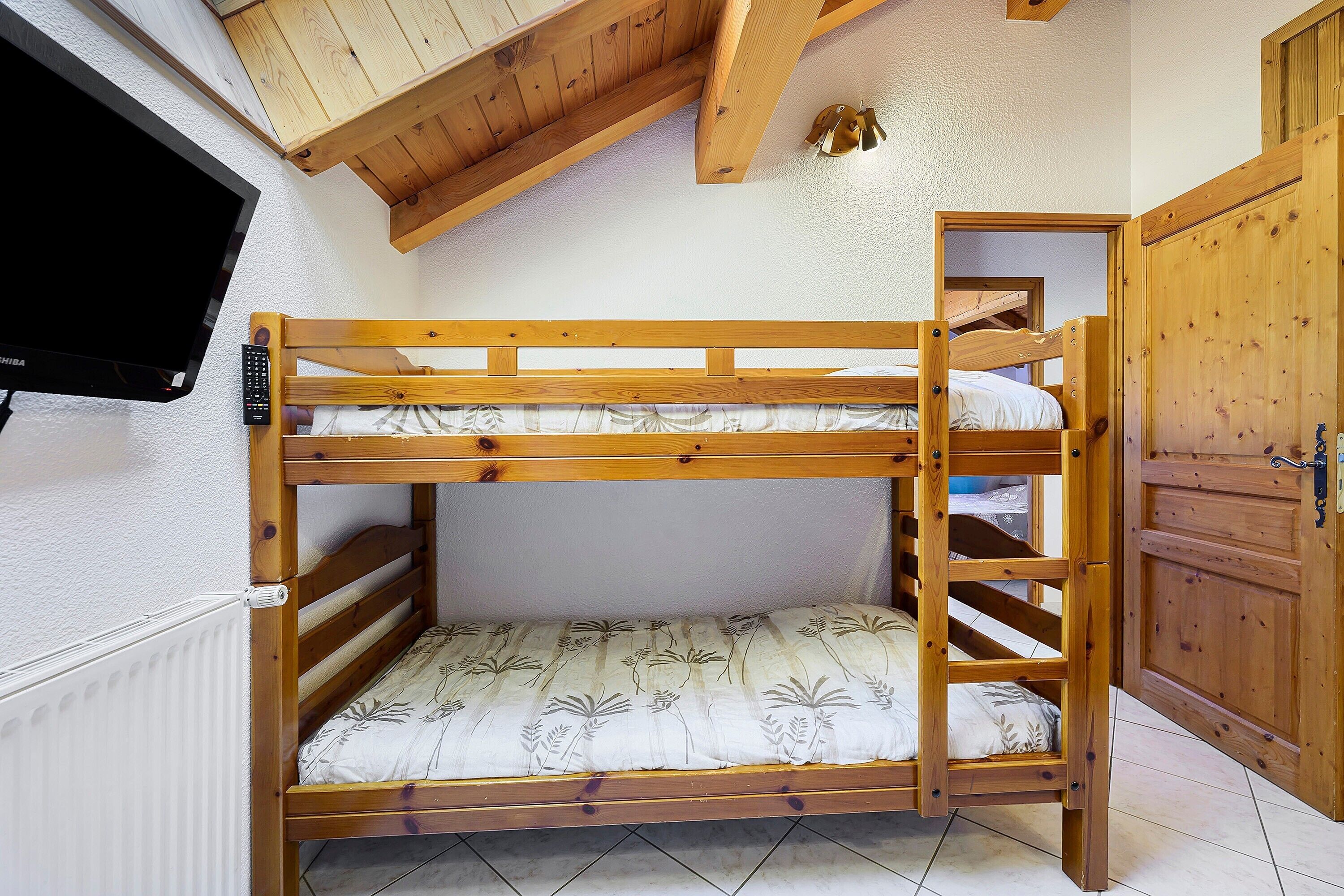 Ein Stockbett mit an der Wand montiertem Fernseher, Holzbalkendecke und einem Holzschrank.