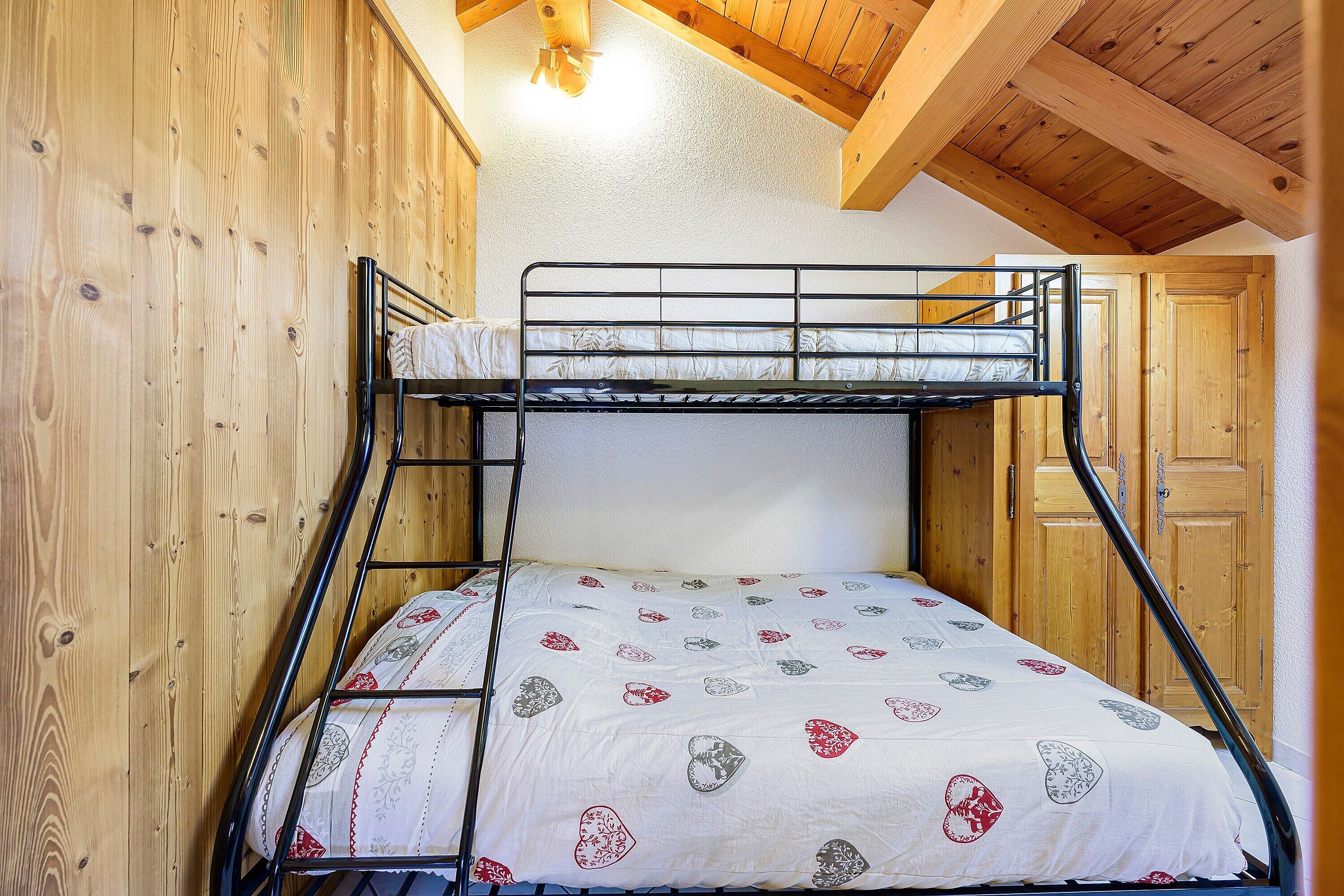A bunk bed with a patterned bedspread, wooden walls, and a sloped ceiling.