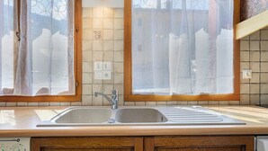 Een keuken met een dubbele spoelbak, houten kastjes en een raam met gordijn.
