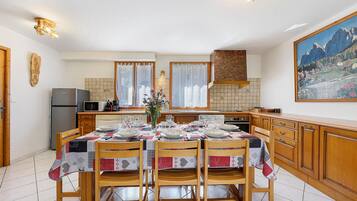 Un coin repas avec une table dressée pour quatre personnes, des chaises en bois, une cuisine en arrière-plan et un tableau accroché au mur.