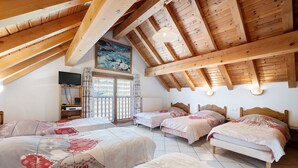 Ein Schlafzimmer mit vier Betten, Holzbalken, einem Gemälde, einem Fernseher und einem Fenster mit Vorhängen.