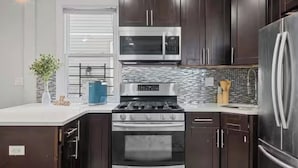 A modern kitchen with dark wood cabinets, stainless steel appliances, and a tiled backsplash.