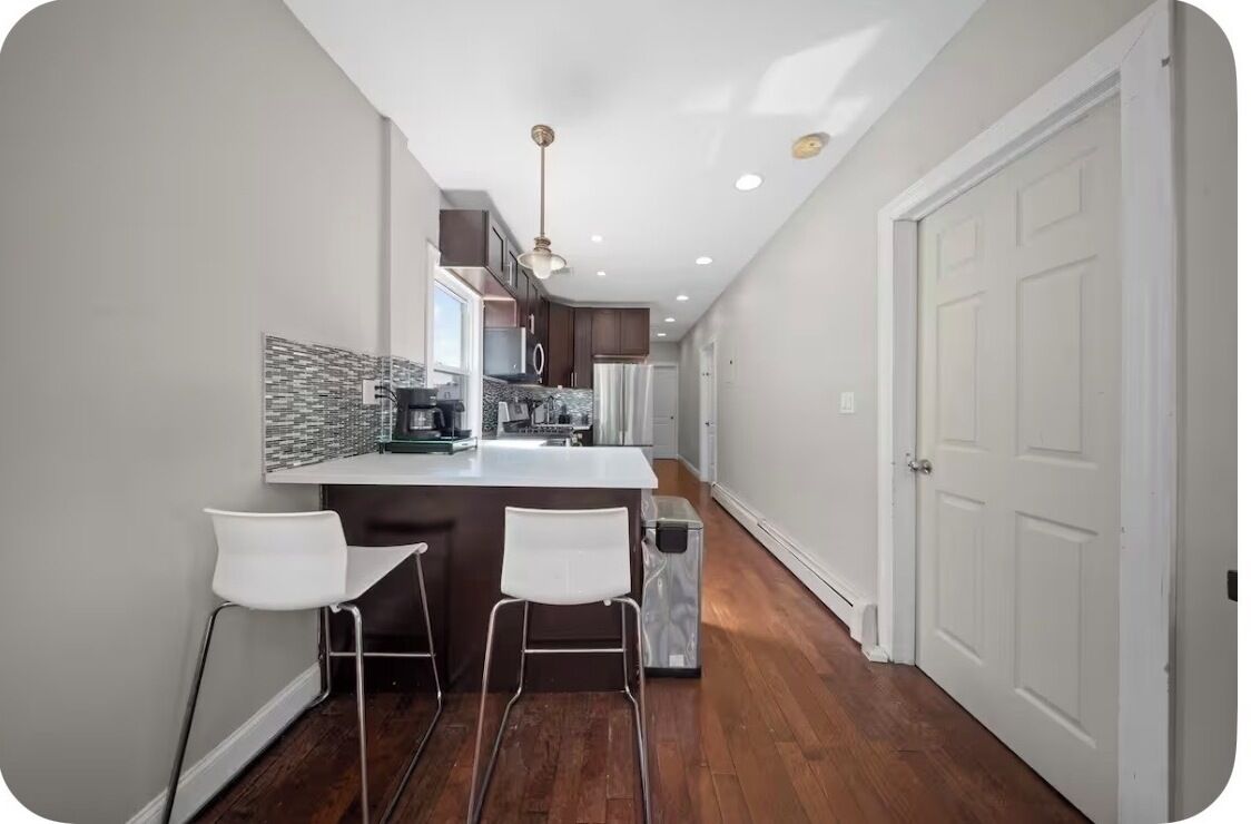 A modern kitchen with a central island, two bar stools, and a pendant light.