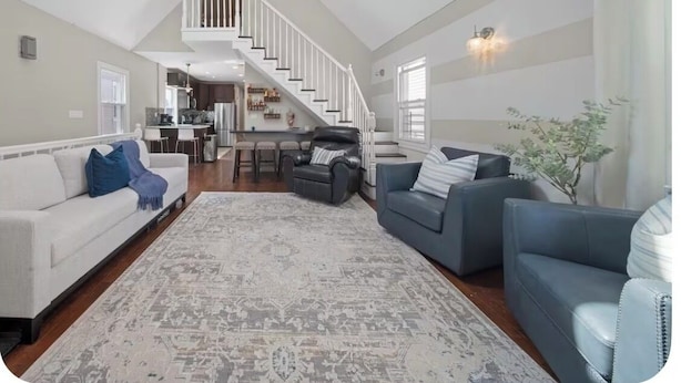 A spacious living area with a high ceiling, a staircase, and a kitchen in the background.