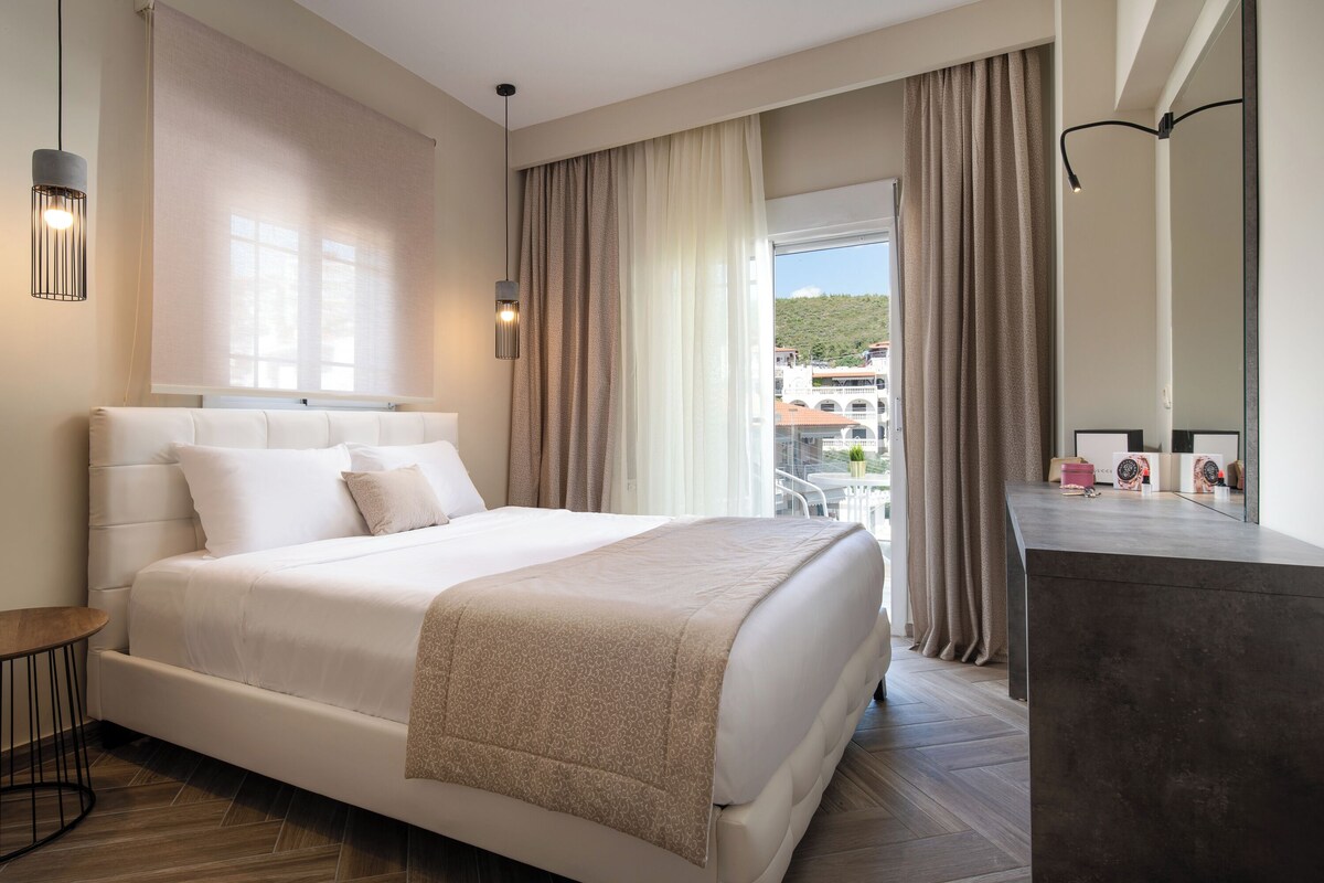 A modern hotel room with a large bed, a bedside table, a desk, and a view of the city.