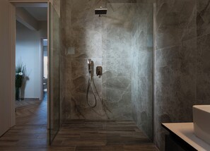Une douche moderne avec une porte en verre, un mur en marbre et un plancher en bois.