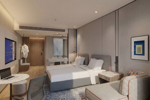Et moderne hotelværelse med en stor seng, et skrivebord med en bærbar computer, en stol, et lille bord og en sofa.