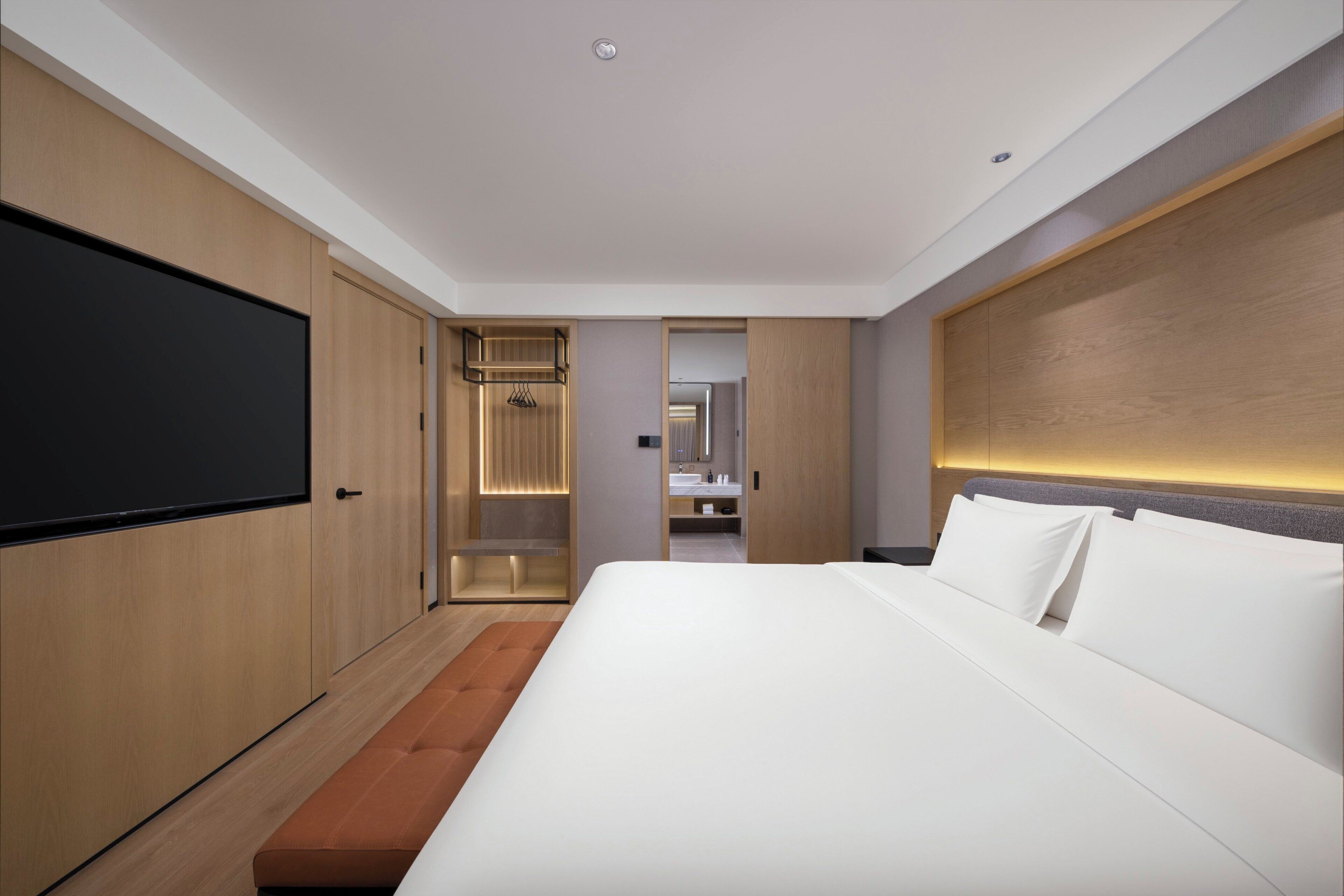 A modern hotel room with a large bed, wooden wardrobe, and a television.