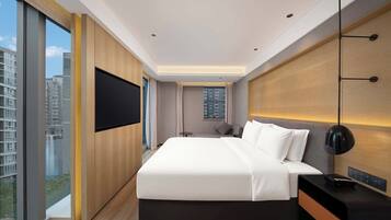 A modern hotel room with a large bed, a TV mounted on the wall, and a view of the cityscape.