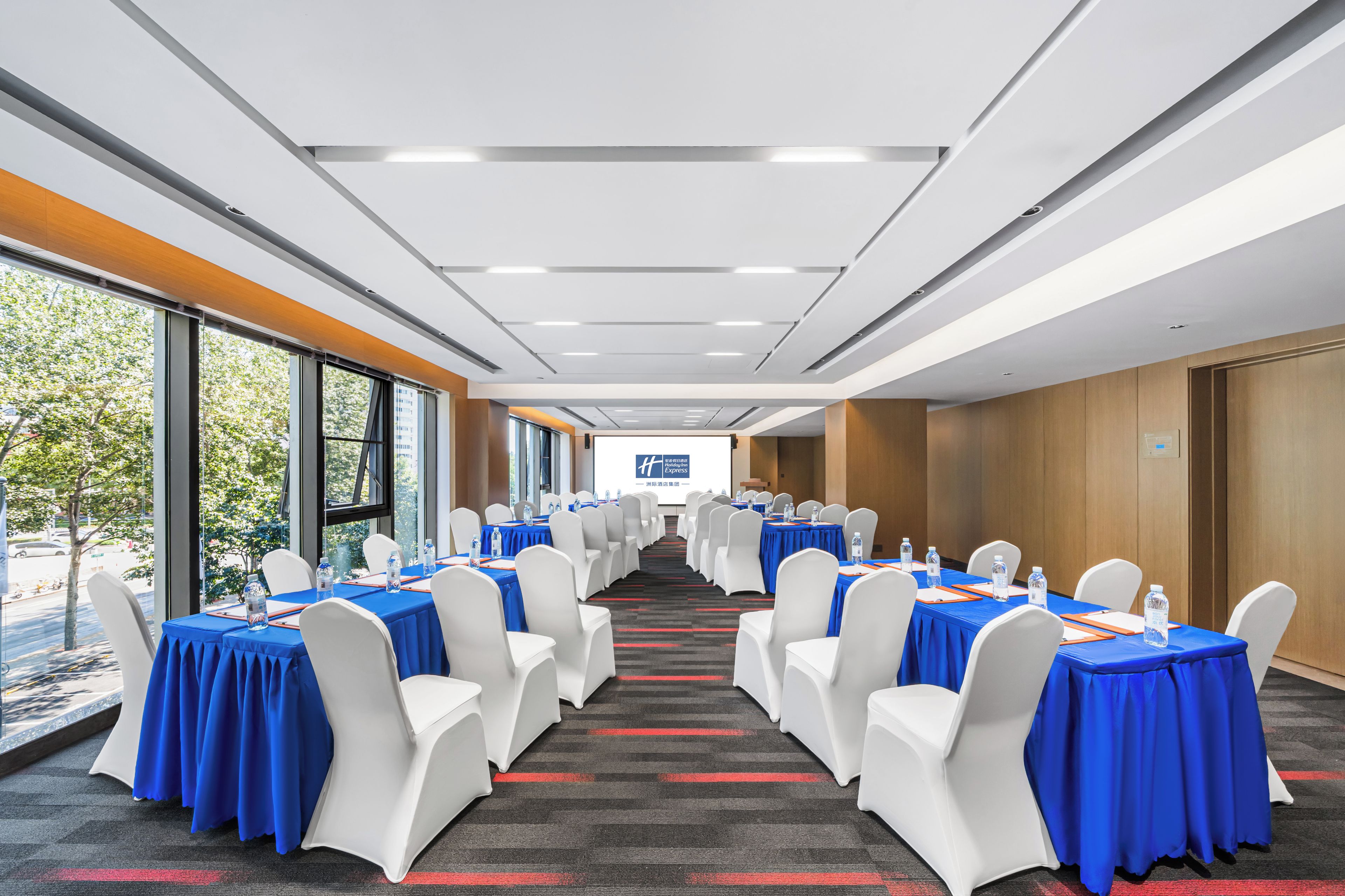 A conference room with tables set for meetings, white chairs, and a large window with a view of trees.