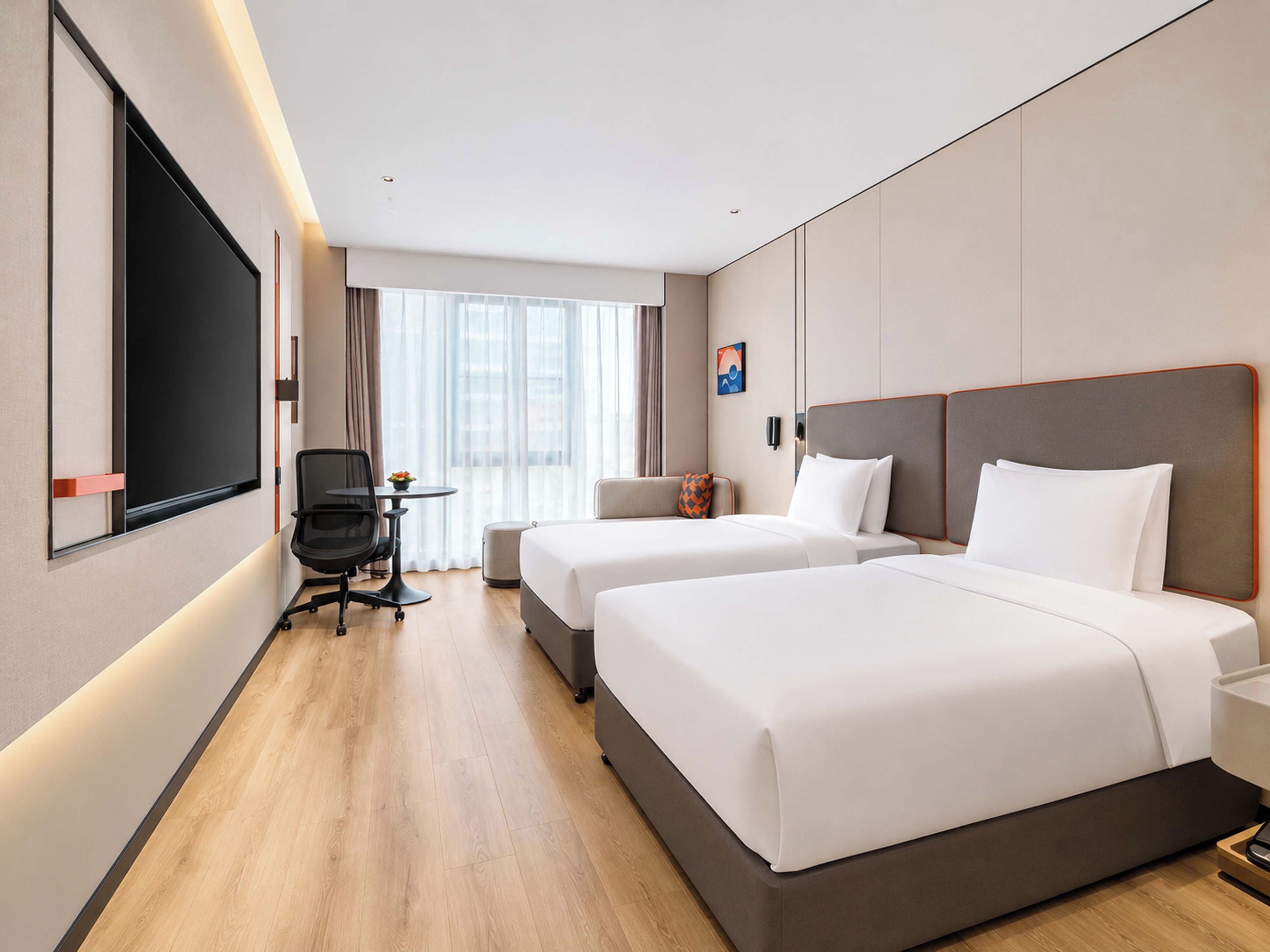 A hotel room with two beds, a desk, a chair, a TV, and a window with curtains.