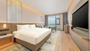 Une chambre d’hôtel moderne dotée d’un grand lit, d’une télévision à écran plat, d’un bureau et offrant une vue sur la ville par la fenêtre.