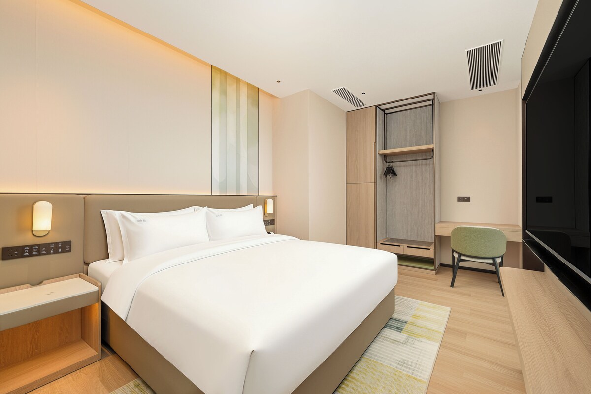 A modern hotel room with a large bed, bedside tables, a desk, and a chair.