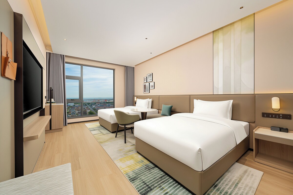A modern hotel room with a large bed, a desk, a chair, and a TV.