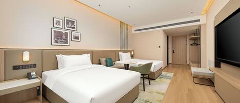 A hotel room with a large bed, a desk, a chair, a television, and a wall-mounted light fixture.