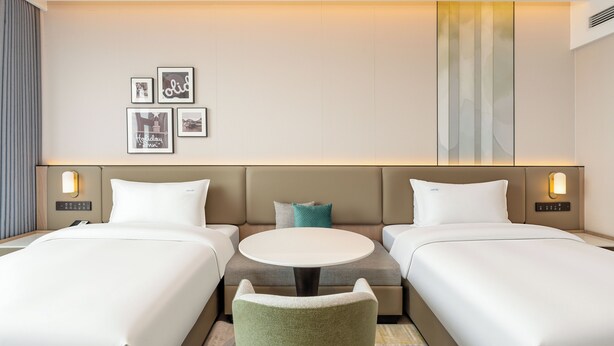 Ett hotellrum med två sängar, en soffa, ett litet bord och väggmonterade lampor.