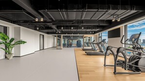 Une salle de sport équipée de tapis de course, d’appareils d’exercice et dotée d’une grande fenêtre offrant une vue sur la ville.