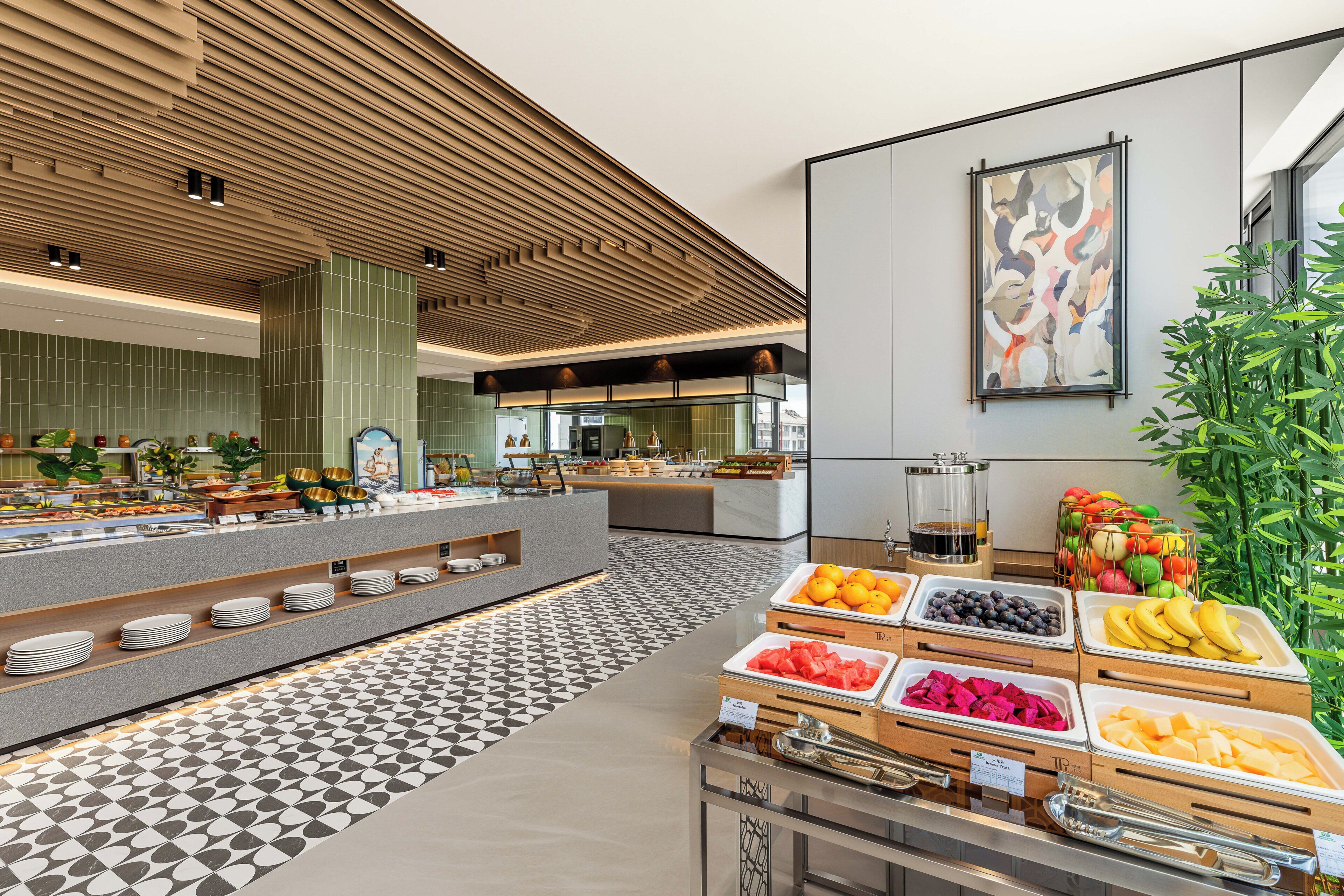Un área de bufé con diversas opciones de comida, una estación de café y un cuadro abstracto grande en la pared.