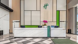 En hotellreception med modern design, utrustad med en bänkskiva i marmor, en grön accentvägg och en skylt som visar vilka tjänster som ingår i paketen ”Diamond Elite” och ”Platinum Elite”.