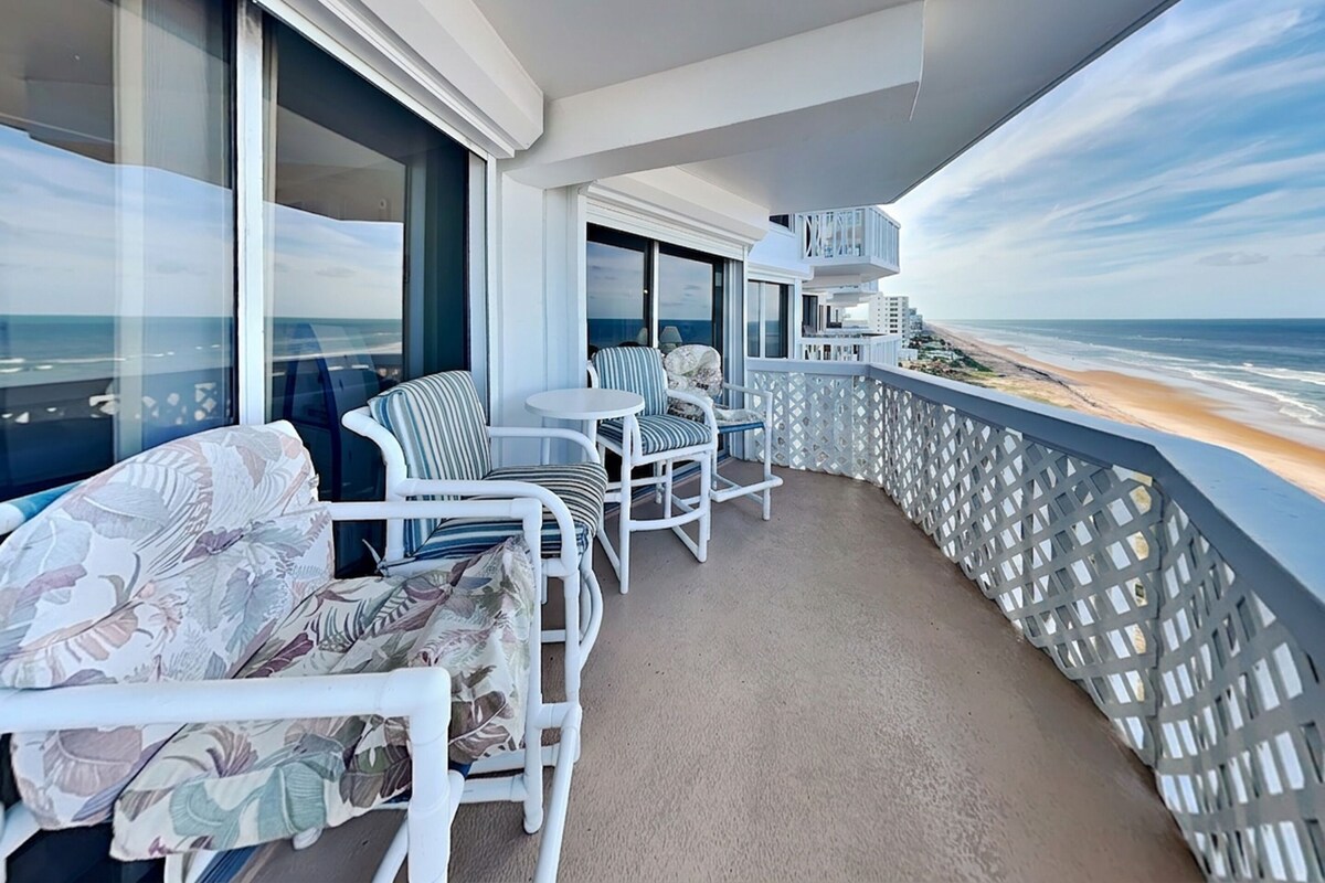 A balcony with white wicker furniture, a small table, and a view of the beach.
