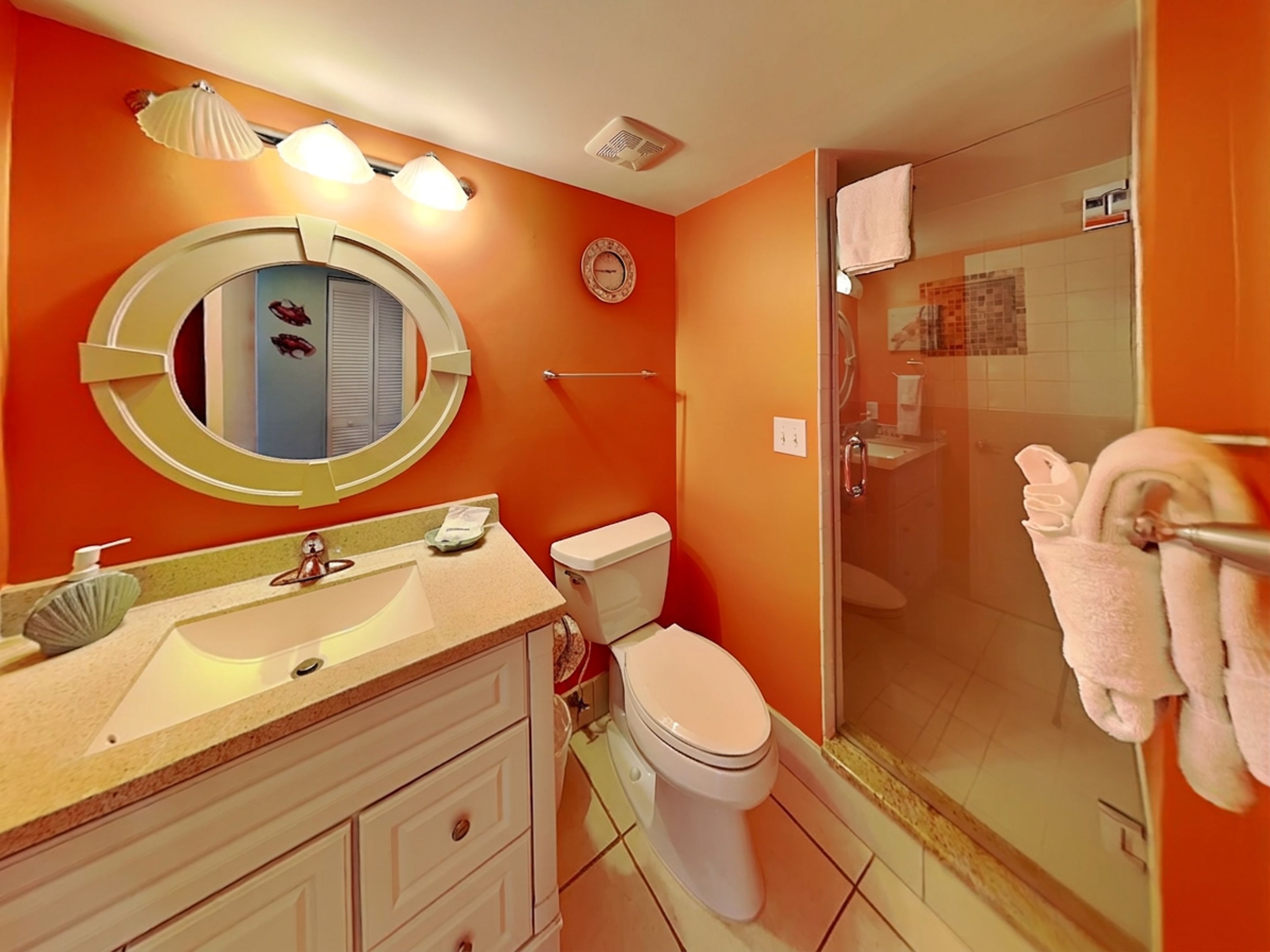 Une salle de bain avec un miroir rond, des toilettes, un lavabo et une douche s éparée par une paroi en verre.