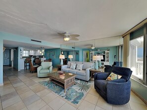 A spacious living area with a sofa, armchairs, a coffee table, and a dining area with chairs and a kitchen in the background.