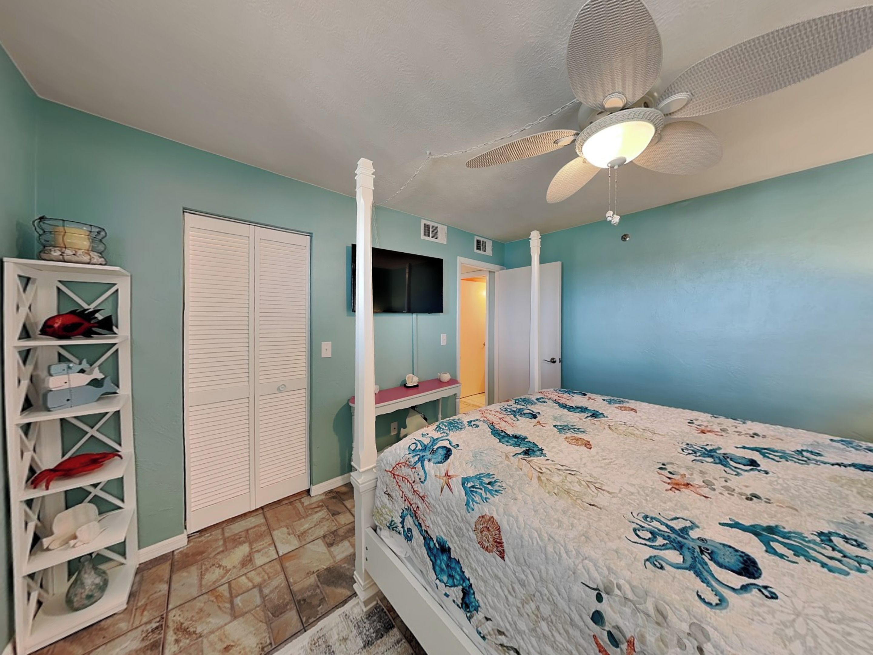 A bedroom with a bed, a ceiling fan, a wardrobe, and a shelf with decorative items.