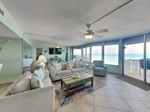 A spacious living room with a sofa set, a coffee table, and a television. There is a balcony with a view of the ocean. - Oceanside Retreat 804-805 (Ormond Beach)