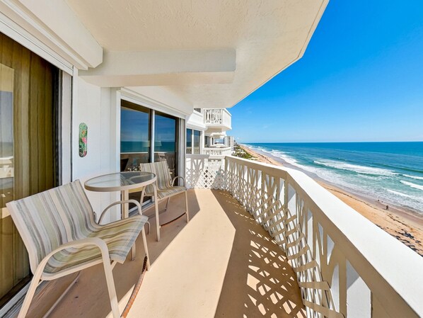 A balcony with a table and chairs, overlooking a beach and ocean.
