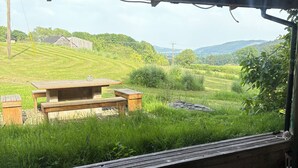 A rustic outdoor seating area with a wooden table and benches, overlooking a lush green landscape with hills and a clear sky. - Walnut Tree Lodge With hot tub (Presteigne)