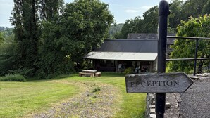A rustic wooden signpost with 'RECEPTION' and 'MORE PARKING' directions, a gravel path, a grassy area, and a building with a metal roof in the background. - Walnut Tree Lodge With hot tub (Presteigne)