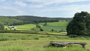 A rural landscape with a wooden bench, rolling green fields, and a distant building. - Walnut Tree Lodge With hot tub (Presteigne)