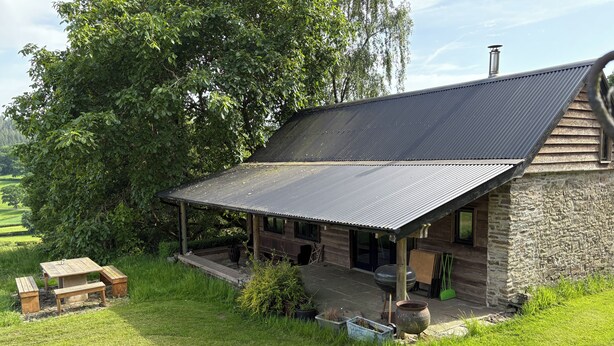 A rustic cabin with a covered porch, a stone exterior, and a grassy yard. - Walnut Tree Lodge With hot tub (Presteigne)