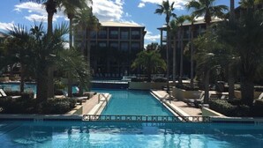 A swimming pool with lounge chairs and palm trees, surrounded by a building with multiple floors.