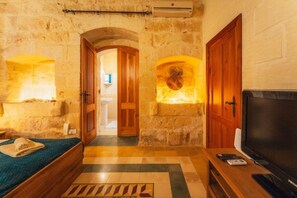 A stone-walled room with a bed, a television, and a stone fireplace. - Authentic Xagħra Farmhouse with Private Pool (Xagħra)