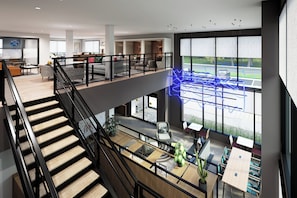 A modern hotel interior with a staircase, seating areas, and large windows offering views of the street. - Atwell Liberty Kansas City East by IHG (Liberty)