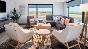 A modern living room with a sofa, chairs, a coffee table, and a large window offering a view of the landscape. - Atwell Suites Liberty - Kansas City East by IHG (Liberty)