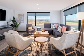 Ein modernes Wohnzimmer mit einer Couch, Sesseln, einem Couchtisch und einem großen Fenster mit Blick auf die Landschaft.