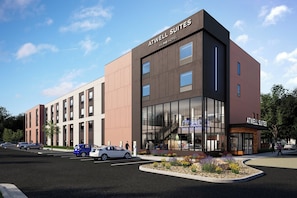 En moderne bygning med skiltning 'ATWELL SUITES', store vinduer og en parkeringsplads med biler.