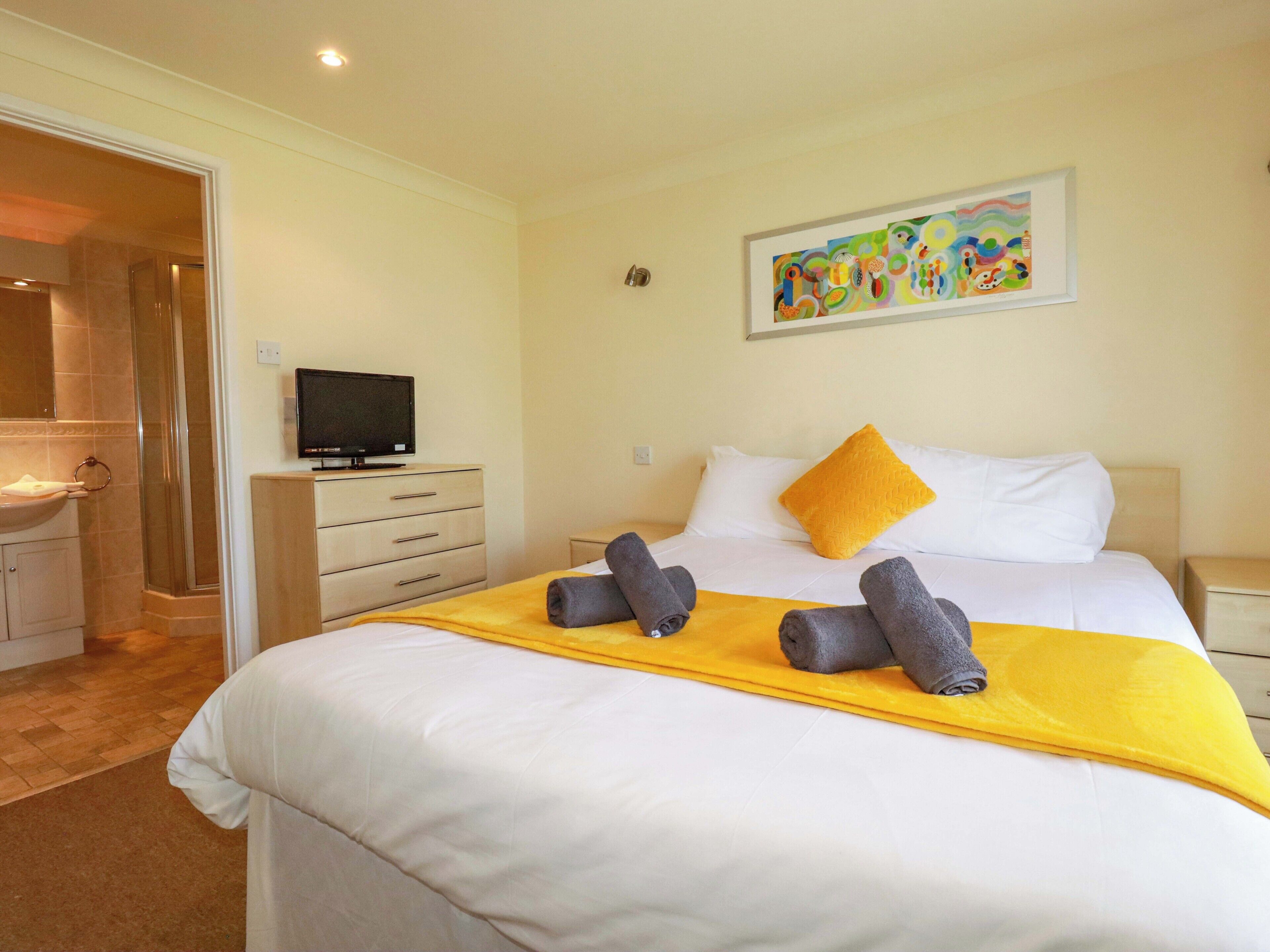 A hotel room with a bed, a television, a bathroom, and a painting on the wall.